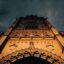 The front face of a gothic church lit up at night against a cloudy and moody sky.