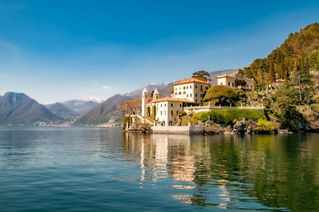 Pristine glassy waters of Como Lake reflect waterfront houses and mountains under a blue sky.