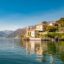 Pristine glassy waters of Como Lake reflect waterfront houses and mountains under a blue sky.