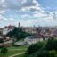 An aerial view of Lublin city with trees and green parklands in the foreground and heritage buildings with grey and terracotta roofs in the background.