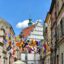A street in Lublin lined with beige and pink heritage buildings with lots of colourful flags hung across the street between the buildings.