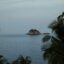 Cloud covered sky over palm trees and ocean waters with a small island in the distance.