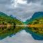 A cloud covered sky and colourful trees reflect off the crystal waters of Sylhet, Bangladesh.