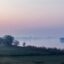 Hazy sunset over water and greenery in Torun, Poland.