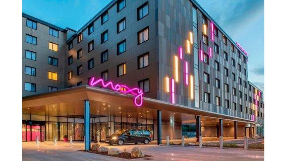 Exterior of Moxy London Hotel in the evening. Picture taken from the street, showing a pink "Moxy" sign.