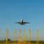 A plane takes off above yellow metal towers at Charleroi Airport.