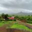 An image of a farm house surrounded by greenery with a grey sky and a mountain range in the distance.