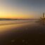 The sun setting over a calm beach with a city buildings in the far distance.