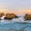 Coastal waters of Preveza crashing against large rocks under a sunset sky.