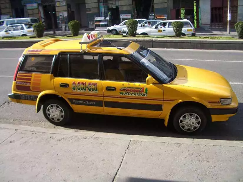 A yellow station-wagon taxi, with green and red signage displayed along the sides of the vehicle, parked on the street