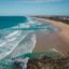 An aerial view of the coastline along the Sunshine Coast with crystal clear blue water and golden sands.