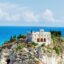 A view of Santa Maria dell'Isola monastery set atop a rocky mountain outcrop against the background of a vibrant blue ocean..