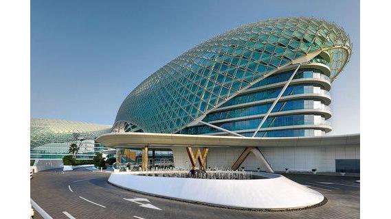 A glass rounded hotel building, with a large W on the front and blue skies above.