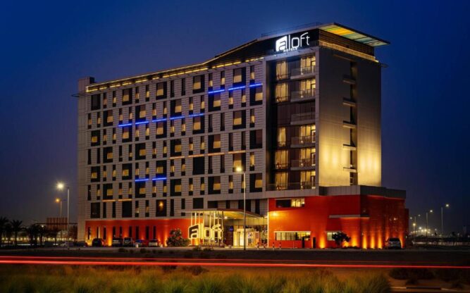 Aloft hotel near Al Maktoum Dubai Airport illuminated at night, showcasing its modern architecture, glowing windows, and convenient location for travelers.