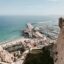 View of the coast in Alicante, showing a large historical wall, with the city below, and a large body of water.