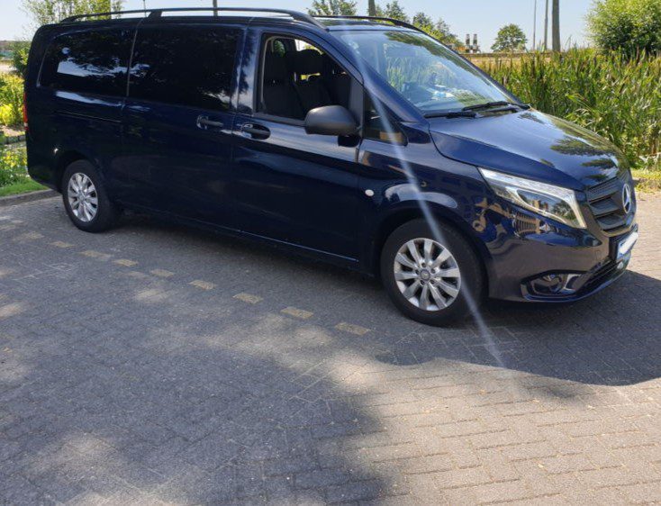 A black Amsterdam Airport taxi minivan parked in an outdoor parking space.