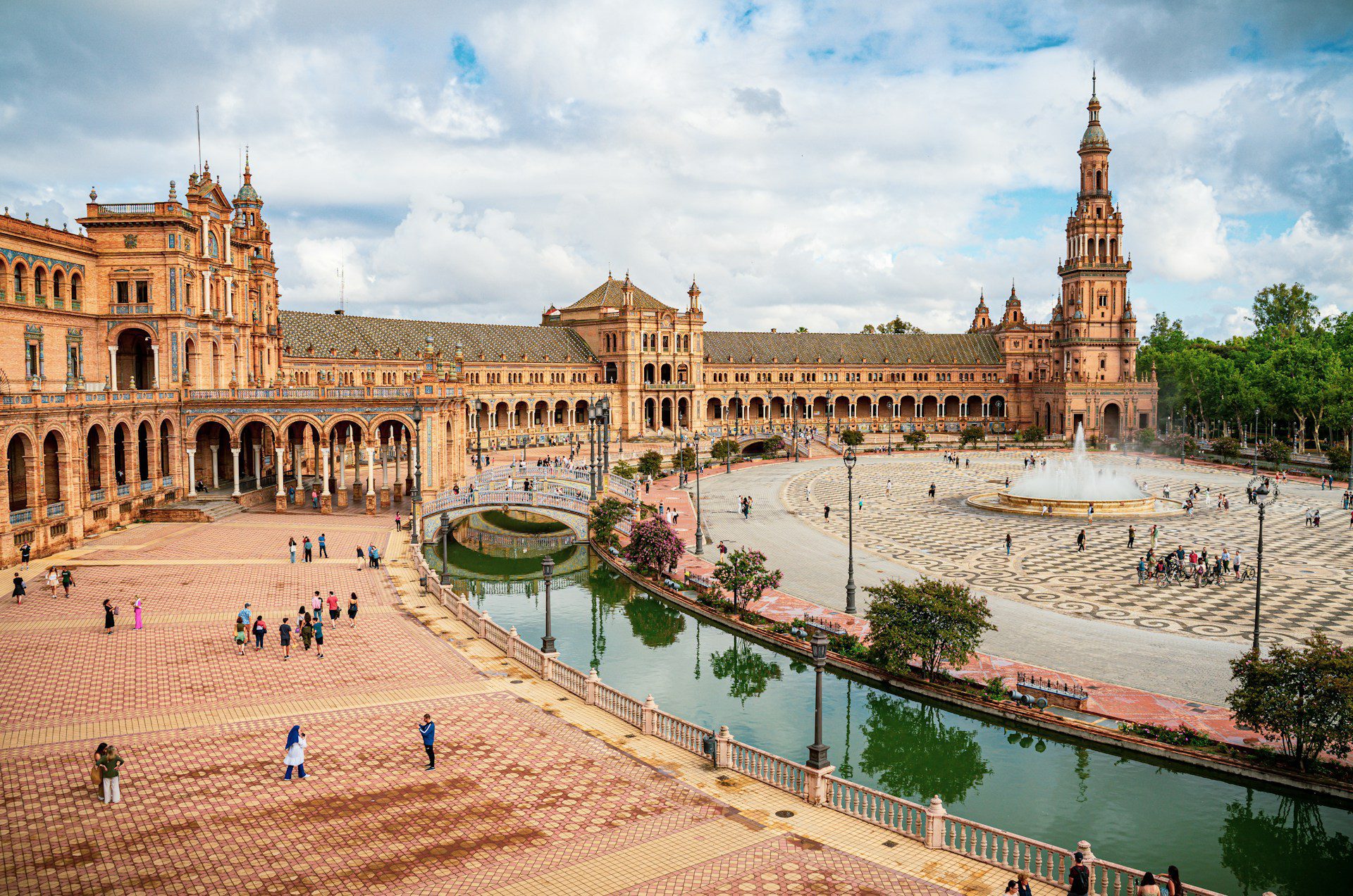 View of a park in central Seville, with terracotta buildings and a body of water with a bridge.