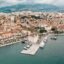 Aerial view of coastal Split, showing the port and buildings, with mountains in the background and water in the foreground.