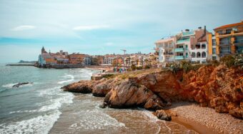 View of Sitges on the coast, with homes lining the waterfront and and blue skies above.