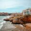 View of Sitges on the coast, with homes lining the waterfront and and blue skies above.