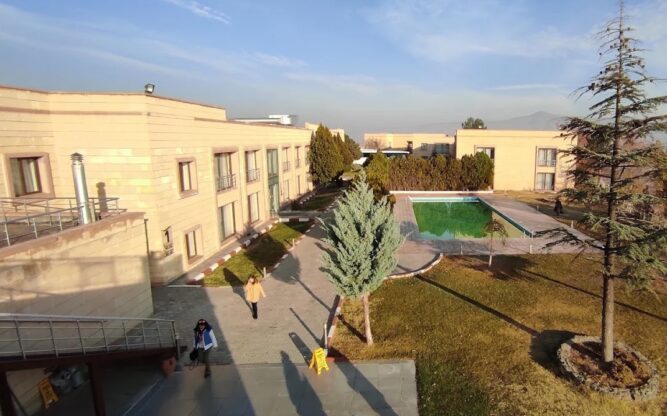 A view of the courtyard at Cappadocia Plus Hotel near Nevsehir Airport with a pool, some trees and people walking in warm clothes.
