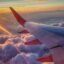 tail of a plane passes over a colorful cloudy sky and a bright orange sun
