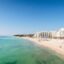 A panoramic view of the Cancun Hotel Zone showing modern beachfront resorts with white façades lining a pristine sandy beach and turquoise water under a clear blue sky — a popular destination for travelers making the journey from Cancun Airport to Hotel Zone.