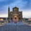 Evening view of the Ta’ Pinu Basilica in Gozo, illuminated against a cloudy sky, with statues lining the entrance path — a popular landmark often visited by travelers going to Gozo from Malta Airport.