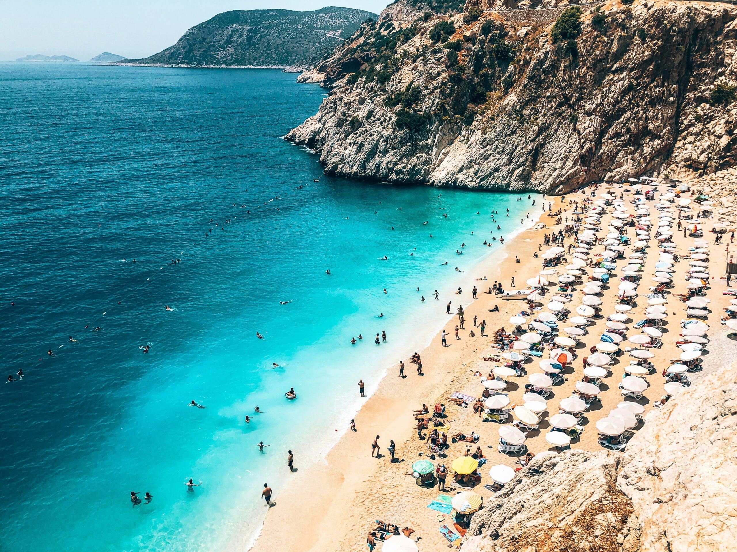 A golden sandy beach covered in beach chairs surrounded by crystal blue waters and large rocky cliffs.