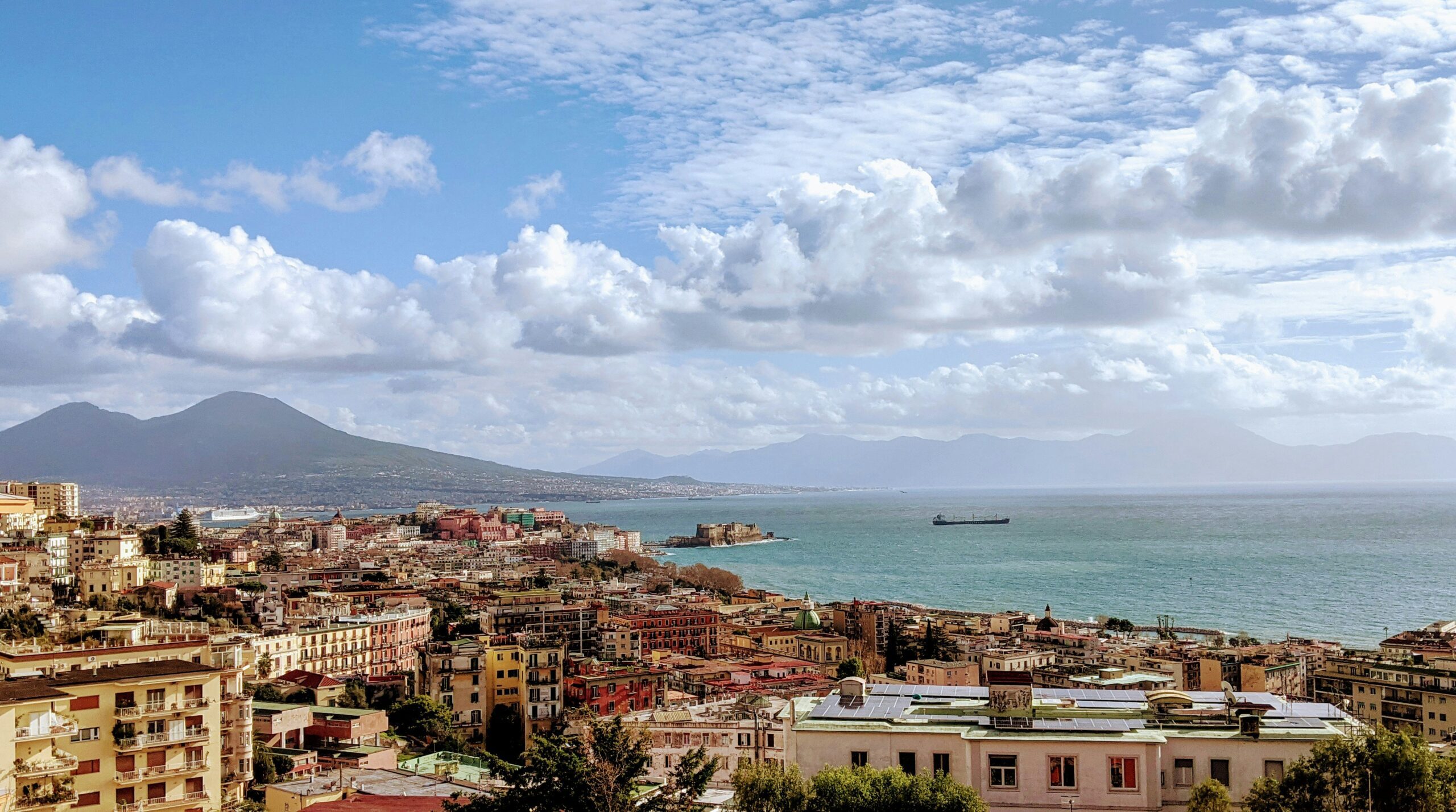 A view of Naples coastline filled with houses and a mountain in the background