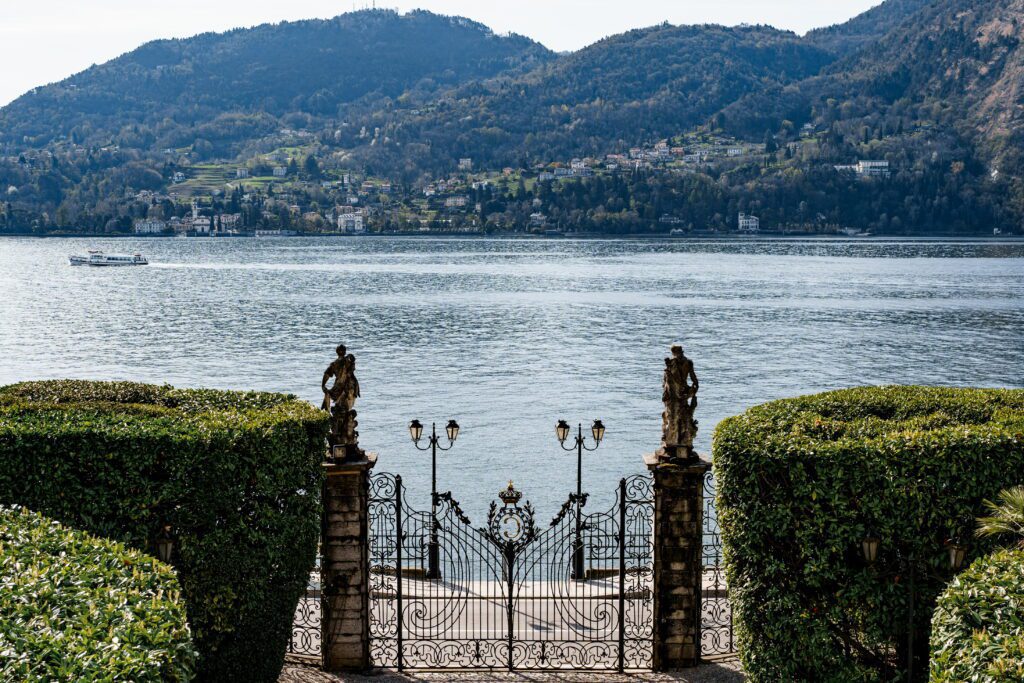 Elegant wrought iron gates overlooking Lake Como in Italy with mountains in the background, a premier location featured in our Devil Wears Prada 2 travel guide.