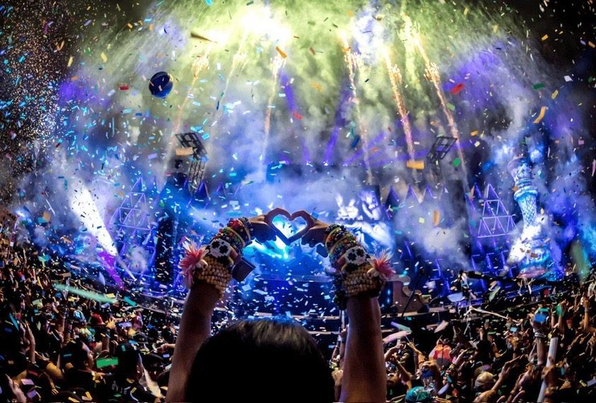 Large crowd celebrating at a Eurovision 2026 fan zone party with confetti, fireworks, and heart hand gestures.