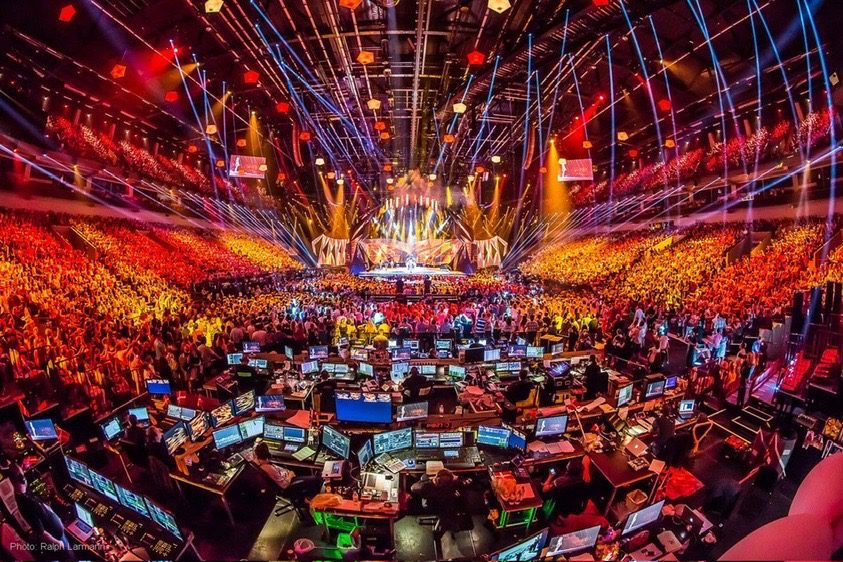 Inside the Eurovision 2026 arena during a live show with vibrant stage lighting, a massive crowd, and the production control desk in the foreground.